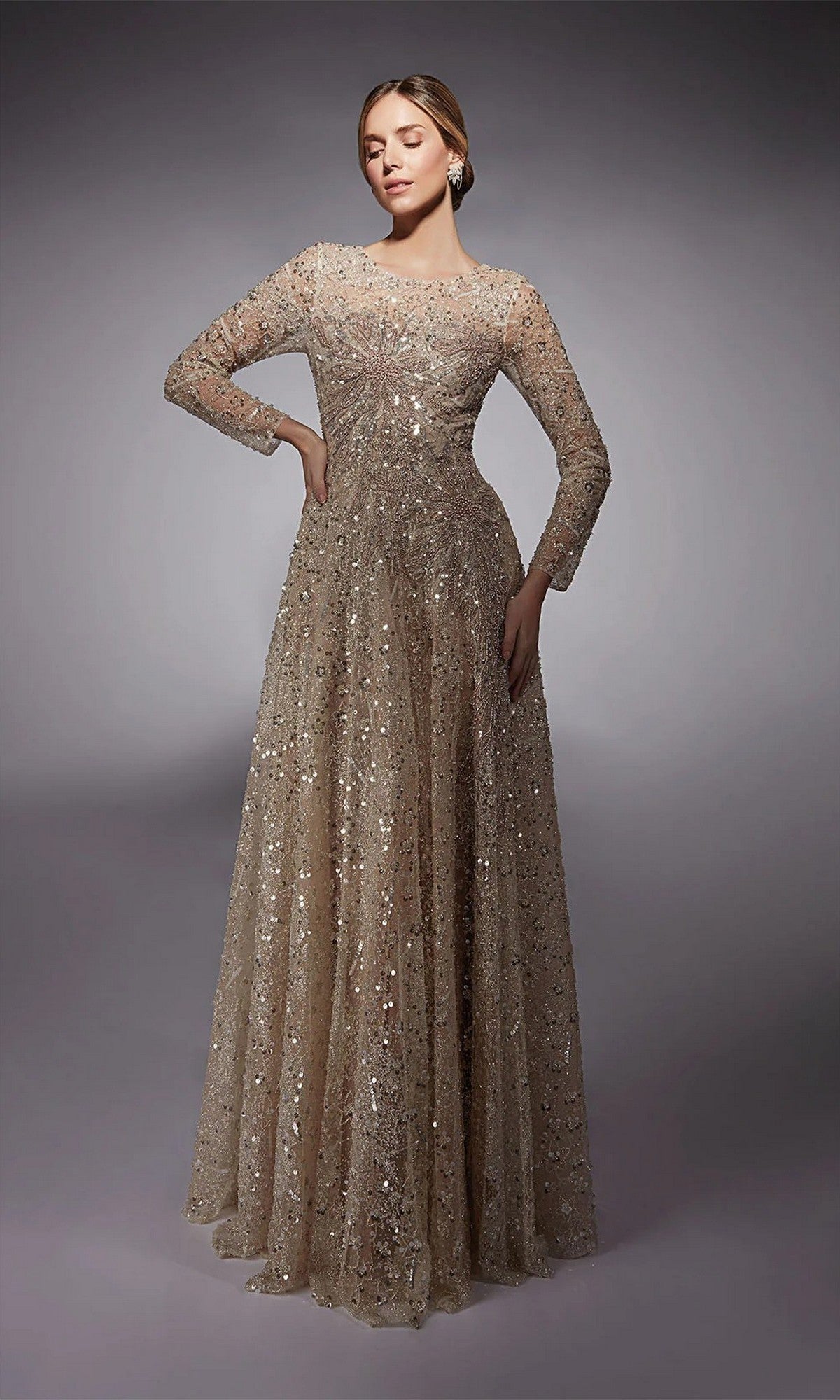A woman poses in the Alyce 27757 long formal dress, featuring long sleeves and sequin-embellished tulle in champagne/cashmere rose—an elegant mother-of-the-bride style—against a plain gray background.
